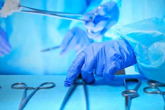 Close-up van van chirurgen handen aan het werk in de operatiekamer afgezwakt in blauw. Medisch team dat operatie uitvoert
