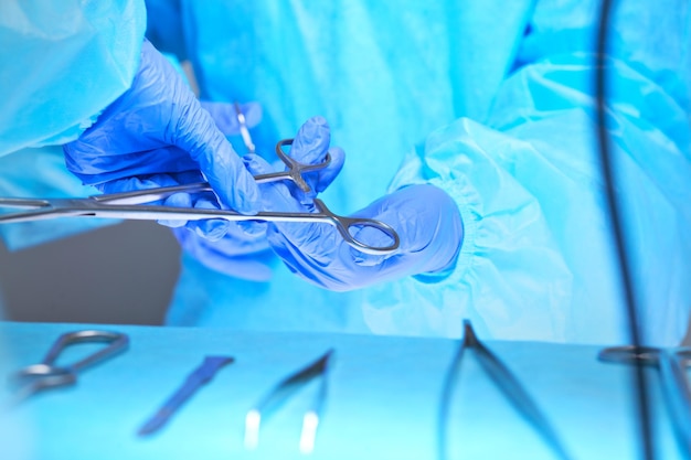 Close-up van van chirurgen handen aan het werk in de operatiekamer afgezwakt in blauw. Medisch team dat operatie uitvoert