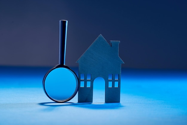 Close-up van vergrootglas en modelhuis op tafel tegen blauwe achtergrond