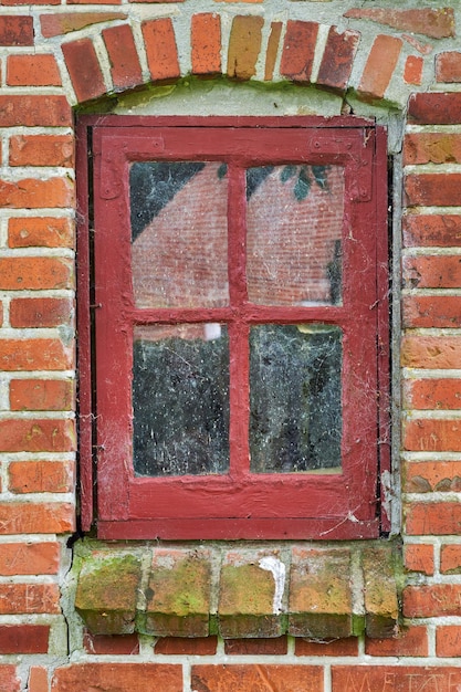 Close-up van verlaten rode raam bedekt met spinnenwebben algen en mos van verwaarlozing armoede en economische crisis Leeg oud woongebouw of huis in een dorp met vochtige schimmel op de vensterbank