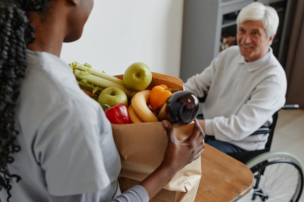 Close-up van verpleegster tas met boodschappen brengen naar senior man in rolstoel