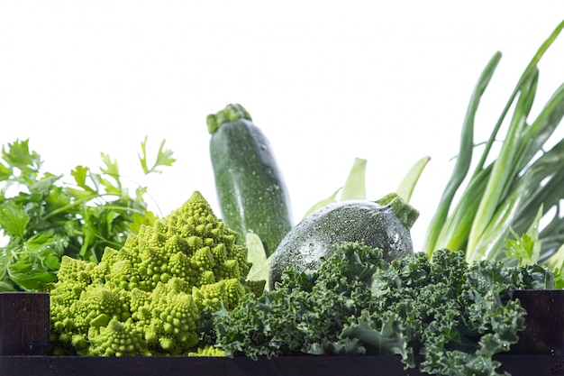 Close-up van verscheidenheid aan verse groene groenten in een houten doos, geïsoleerd op een witte achtergrond.