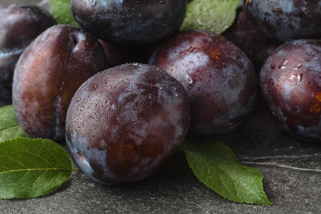 Foto close-up van verse paarse pruimen met druppels op stenen tafel selectieve focus