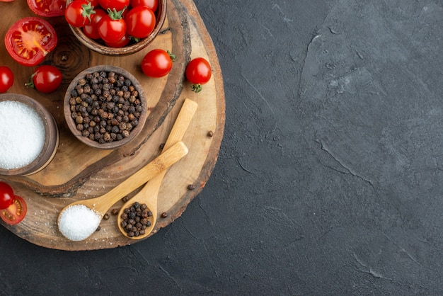 Close-up van verse tomaten en kruiden op een houten bord aan de rechterkant op een zwarte ondergrond met vrije ruimte