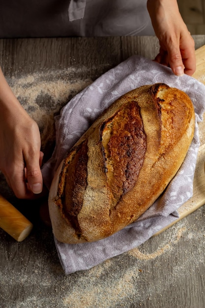 Foto close-up van versgebakken brood in handen op de achtergrond van een houten plank