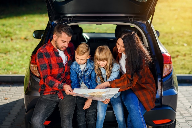 Close up van vreugdevolle aangename familie die samen op vakantie gaan met tienerkinderen en de routekaart gebruiken om het juiste pad op de auto te kiezen