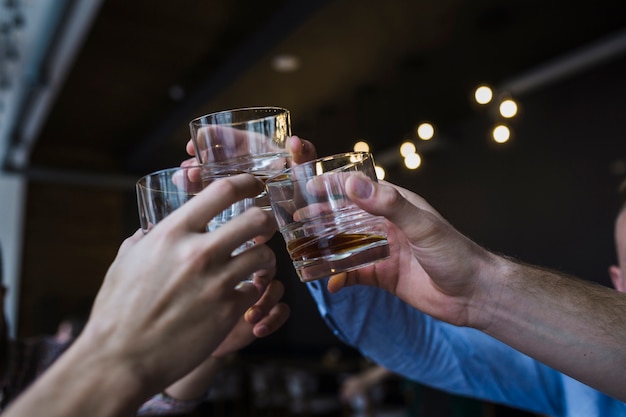 Foto close-up van vriendenhand die toost met glas whisky opheffen