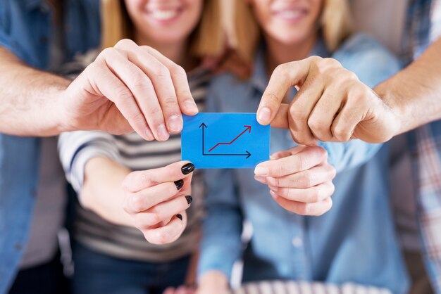 Close-up van vrolijke collega's met een klein blauw papier met stijgende grafiek.