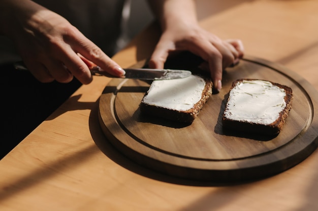 Close-up van vrouw boter het geroosterde roggebrood door veganistische boter. Vrouw boter toast thuis op houten