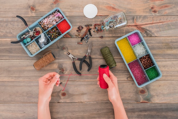 Foto close-up van vrouw die rode garenspoel met creatieve parels met de hand gemaakte materialen op houten bureau houdt