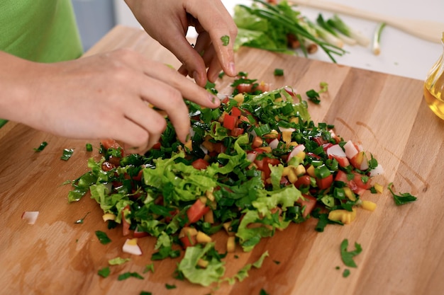 Close up van vrouw handen koken in de keuken. Huisvrouw die verse salade snijdt. Vegetarisch en gezond kookconcept.