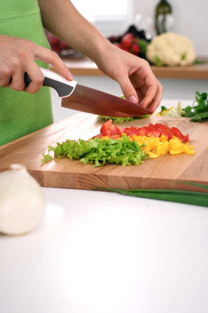 Close up van vrouw handen koken in de keuken. Huisvrouw die verse salade snijdt. Vegetarisch en gezond kookconcept.