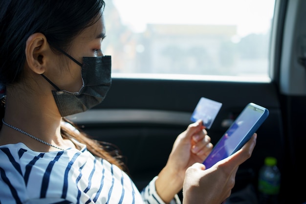 Close-up van vrouw handen met smartphone en creditcard zittend op de achterbank van de auto.
