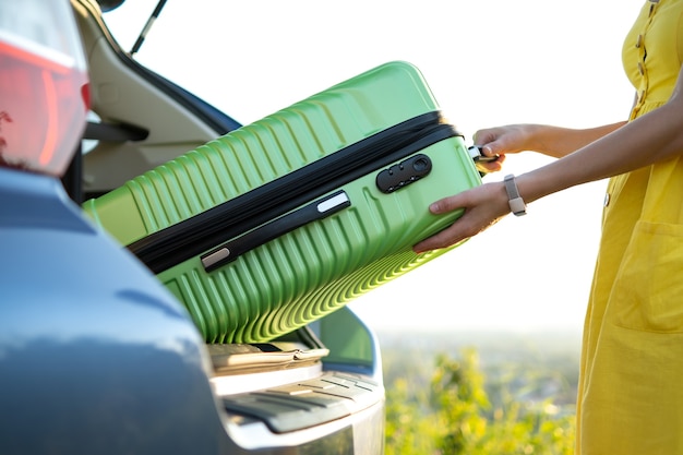 Close up van vrouw handen nemen groene koffer uit auto kofferbak. Reizen en vakanties concept.