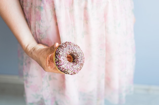 Close-up van vrouw houdt chocolade donut cake. Ongezond junkfood concept op blauwe achtergrond.