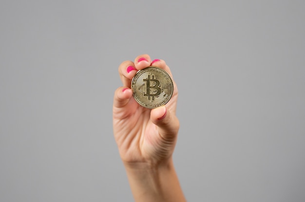 Close up van vrouw houdt in haar hand een gouden bitcoin op grijze achtergrond. Crypto valuta concept.