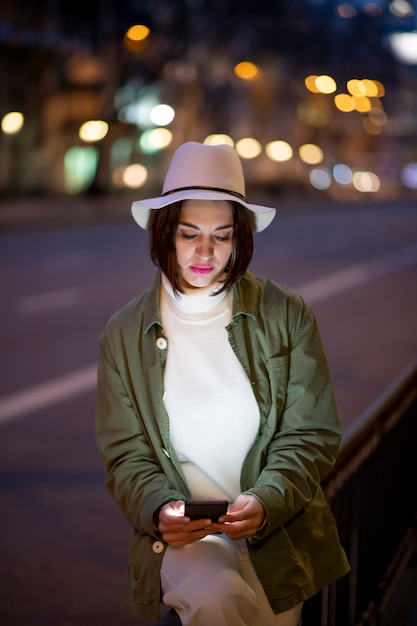 Close-up van vrouw in witte hoed die smartphone gebruikt tijdens het lopen op straat