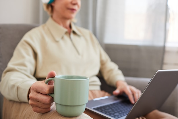 Close-up van vrouw met kopje koffie zittend op de Bank met laptop en koffie drinken in de ochtend