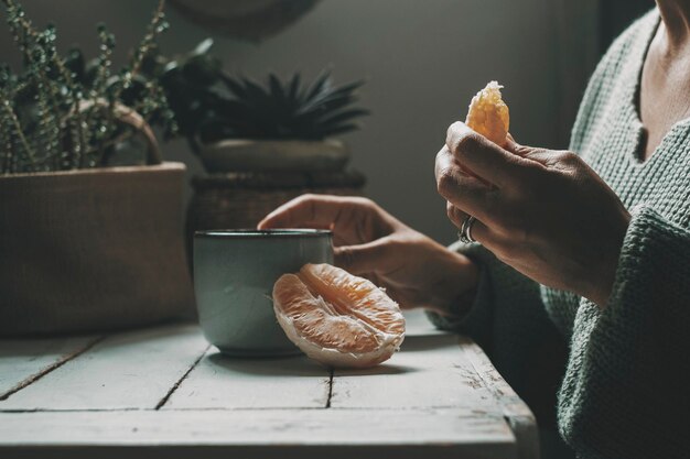 Close up van vrouw oranje fruit eten en kruidenthee of koffie drinken thuis gezonde voeding en drank levensstijl mensen binnen Donkere sfeer kleur groen grijs Ontspanning en genieten van ontspannen binnen