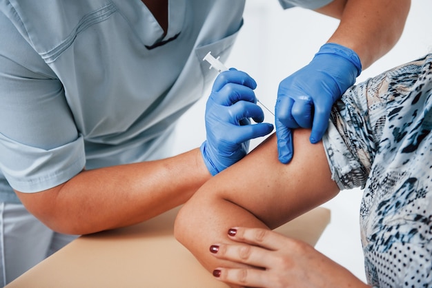 Close-up van vrouwelijke arts die patiënt in de kliniek injecteert met een spuit.