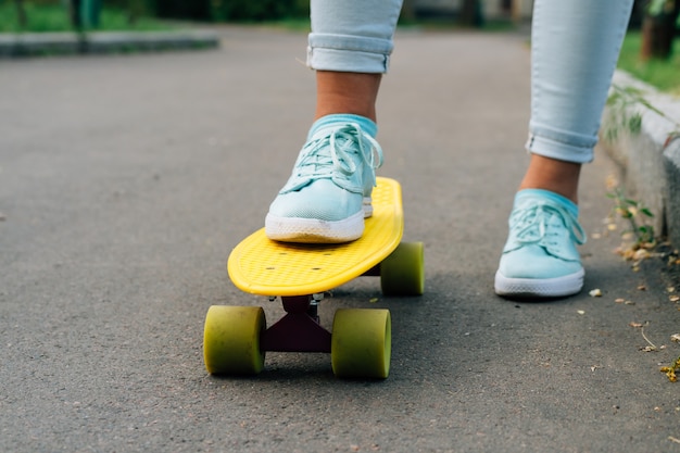 Close-up van vrouwelijke benen in jeans en tennisschoenen die zich op een geel skateboard bevinden