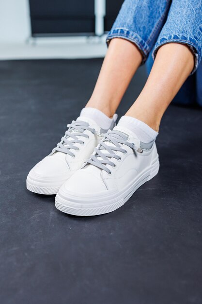 Close-up van vrouwelijke benen in spijkerbroek en casual witte sneakers Comfortabele casual damesschoenen Witte lederen damessneakers