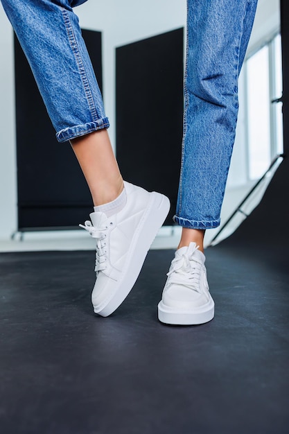 Close-up van vrouwelijke benen in spijkerbroek en casual witte sneakers Comfortabele casual damesschoenen Witte lederen damessneakers