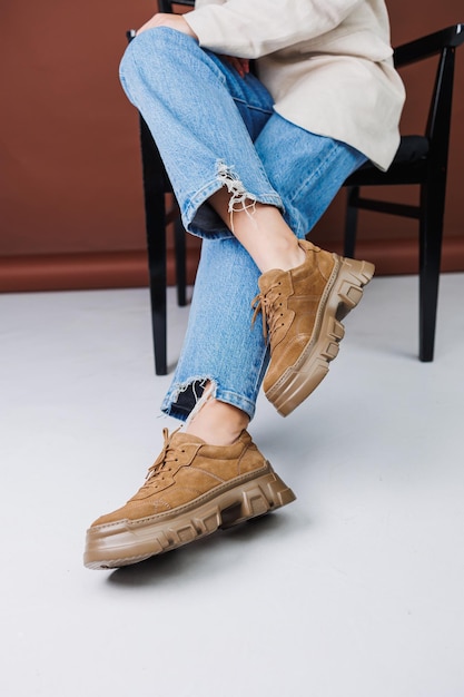 Close-up van vrouwelijke benen in spijkerbroek en suède bruine sneakers Leren casual damessneakers