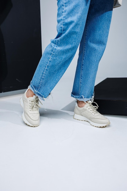 Close-up van vrouwelijke benen in spijkerbroek en witte stijlvolle sneakers Casual damesmode Comfortabele schoenen voor dames Comfortabele zomerschoenen voor dames