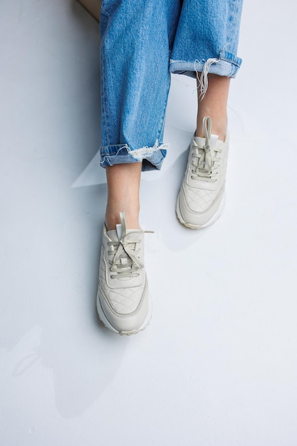 Close-up van vrouwelijke benen in spijkerbroek en witte stijlvolle sneakers Casual damesmode Comfortabele schoenen voor dames Comfortabele zomerschoenen voor dames