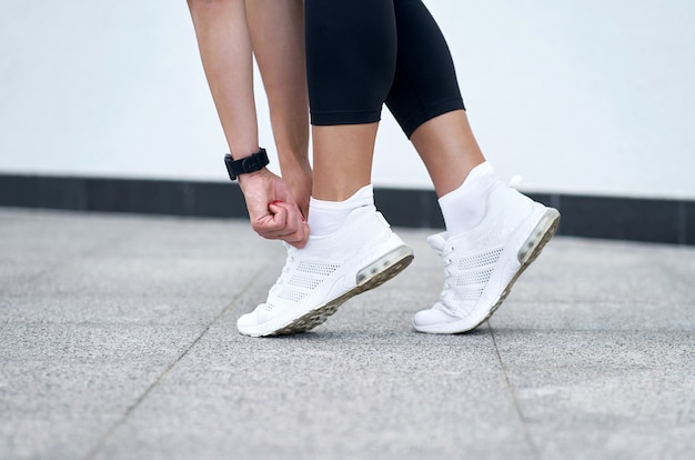 Close-up van vrouwelijke benen in zwarte sportbeenkappen in modieuze witte tennisschoenen. Actieve slanke vrouw op een training. Klaar om te starten.