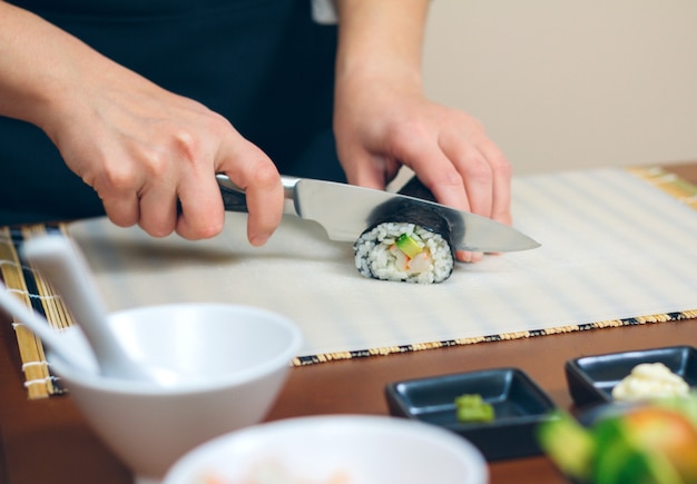 Close-up van vrouwelijke chef-kok die Japanse sushibroodjes met rijst, avocado en garnalen op nori-zeewierblad snijdt