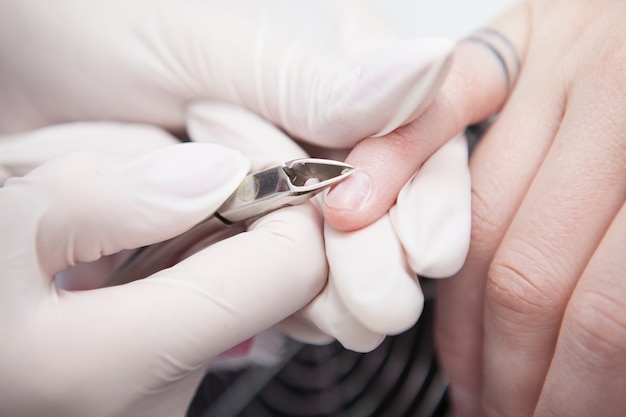 Close-up van vrouwelijke cliënt die nagelriemen heeft verwijderd met een tang door haar manicuremani