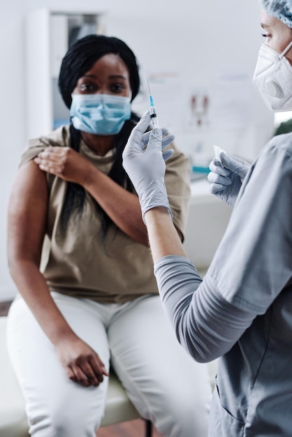 Foto close-up van vrouwelijke dokter in beschermende handschoenen met spuit voor vaccinatie terwijl de patiënt erin zit