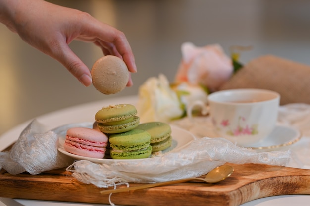 Close-up van vrouwelijke hand Franse macaron plukken uit een plaat op salontafel met tae cup en decoraties