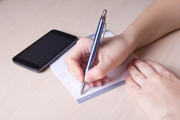 Close up van vrouwelijke hand met pen notebook en slimme telefoon