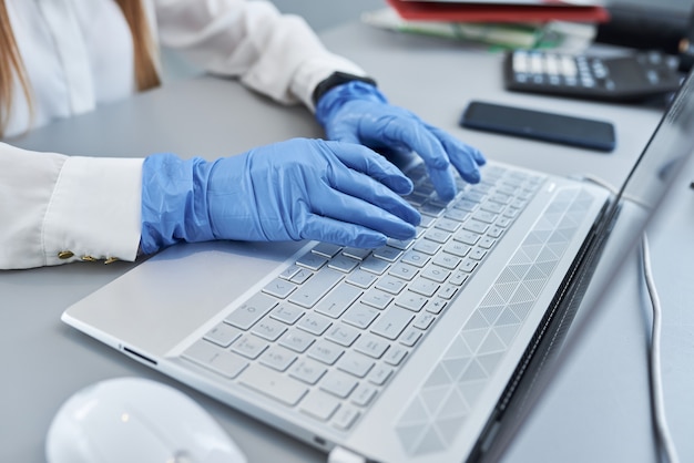 Close up van vrouwelijke handen in blauwe chirurgische handschoenen op laptop toetsenbord.