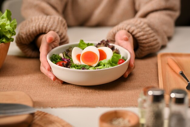 Close-up van vrouwelijke handen met een plaat van salade met gekookte eieren, sla en tomaat op de eettafel