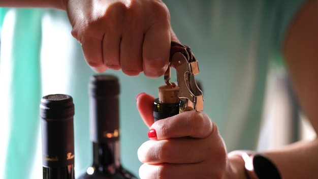 Close-up van vrouwelijke handen met felrode manicure die fles wijn opent met kurkentrekker