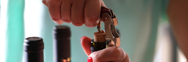 Close-up van vrouwelijke handen met felrode manicure die fles wijn opent met kurkentrekker