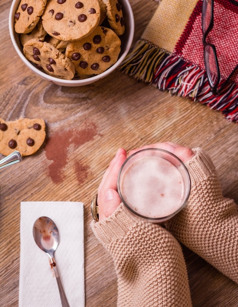 Close-up van vrouwelijke handen met warm drankglas boven een tafel met chocoladeschilferkoekjes op sterrenkom