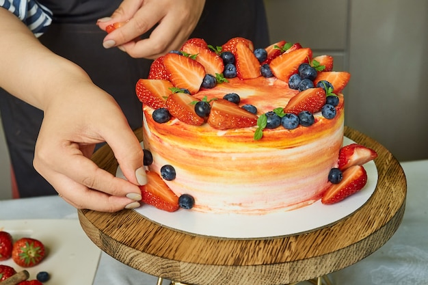 Close-up van vrouwelijke handen versieren zelfgemaakte cake met aardbeien en bosbessen. Thuisbakkerij, klein bedrijf.