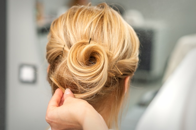 Close up van vrouwelijke kapper styling blonde haren van een jonge vrouw in een schoonheidssalon