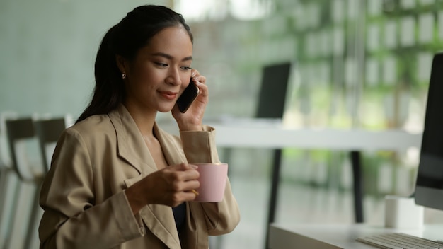 Close-up van vrouwelijke ondernemer praten aan de telefoon tijdens een koffiepauze in kantoorruimte