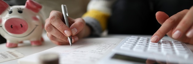 Close-up van vrouwelijke schrijven en boekhouding gezinsbudget. Spaarvarken voor besparingen.