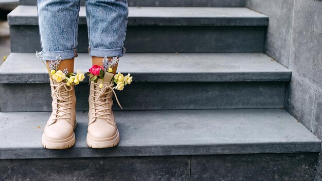 Foto close-up van vrouwelijke voeten in laarzen met verschillende kleurrijke lentebloemen binnen