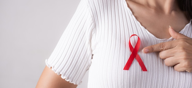 Close-up van vrouwenhand die naar rood kentekenlint op borst richt ter ondersteuning van AIDS-dag.
