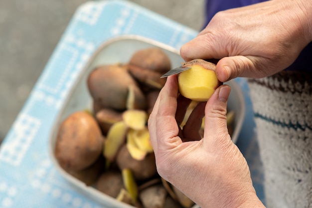 Close-up van vrouwenhanden die aardappels met een keukenmes pellen.