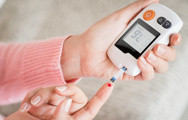 Foto close-up van vrouwenhanden die de bloedsuikerspiegel controleren met een glucosemeter voor diabetestester die wordt gebruikt als medicijn, glycemie, gezondheidszorg en medisch concept.