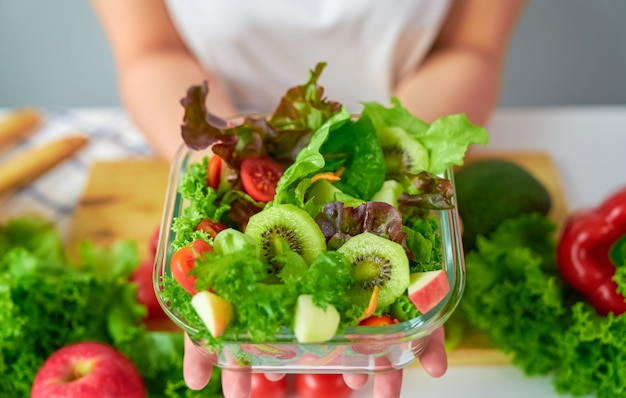 Close-up van vrouwenhanden die saladekom en diverse groene bladgroenten op de lijst tonen bij het huis.